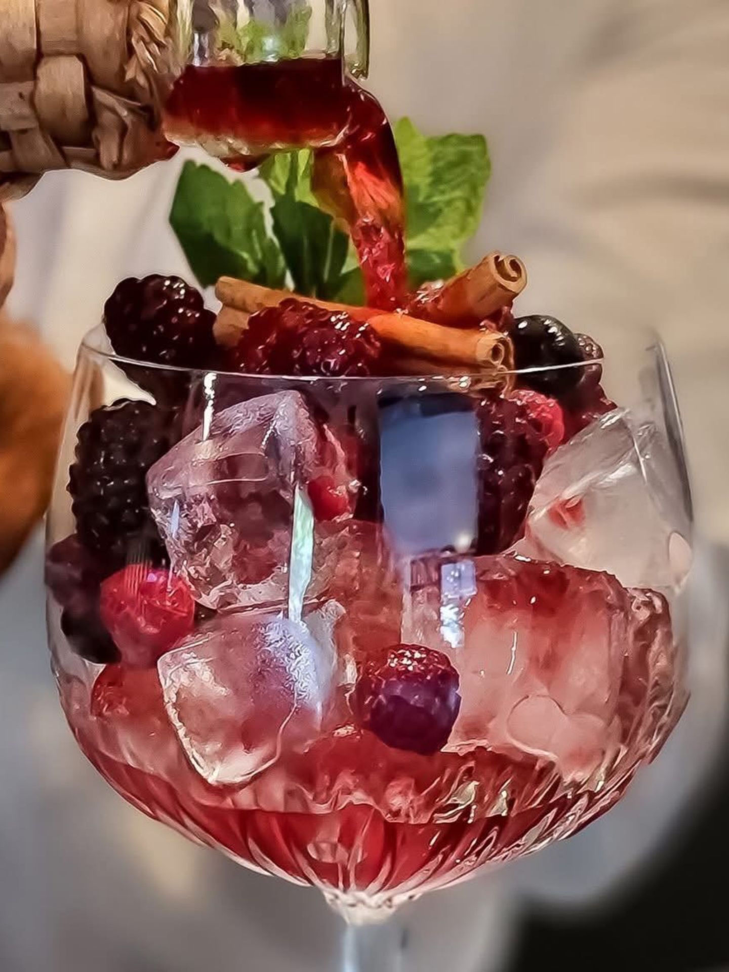 Cocktail rouge aux fruits rouges et glaçons avec canelle, verre transparent, menthe fraîche en arrière-plan, servage en cours