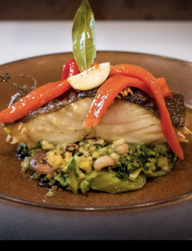 Filet de poisson grillé garni de poivrons rouges, accompagné d'une base de légumes verts et de cacahuètes, présenté dans une