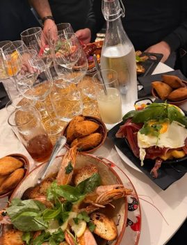 Table de restaurant avec crevettes grillées, croquettes dorées, charcuterie ibérique, verres de vin blanc et eau gazeuse