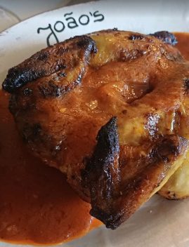 Poulet grillé rôti servi avec sauce brune sur assiette blanche du restaurant João's, garni de basilic frais