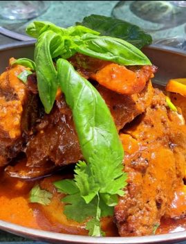 Ragoût de viande portugais aux poivrons jaunes et oranges, garni de basilic frais et coriandre, servi dans un plat en sauce