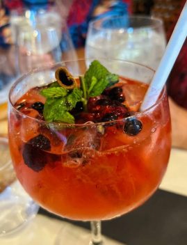 Cocktail rouge garni de myrtilles fraîches, menthe verte et glaçons dans un verre, avec d'autres boissons en arrière-plan